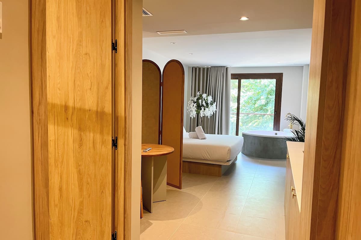 Une chambre d’hôtel moderne avec un lit, une petite table ronde, une baignoire et une fenêtre avec des rideaux.