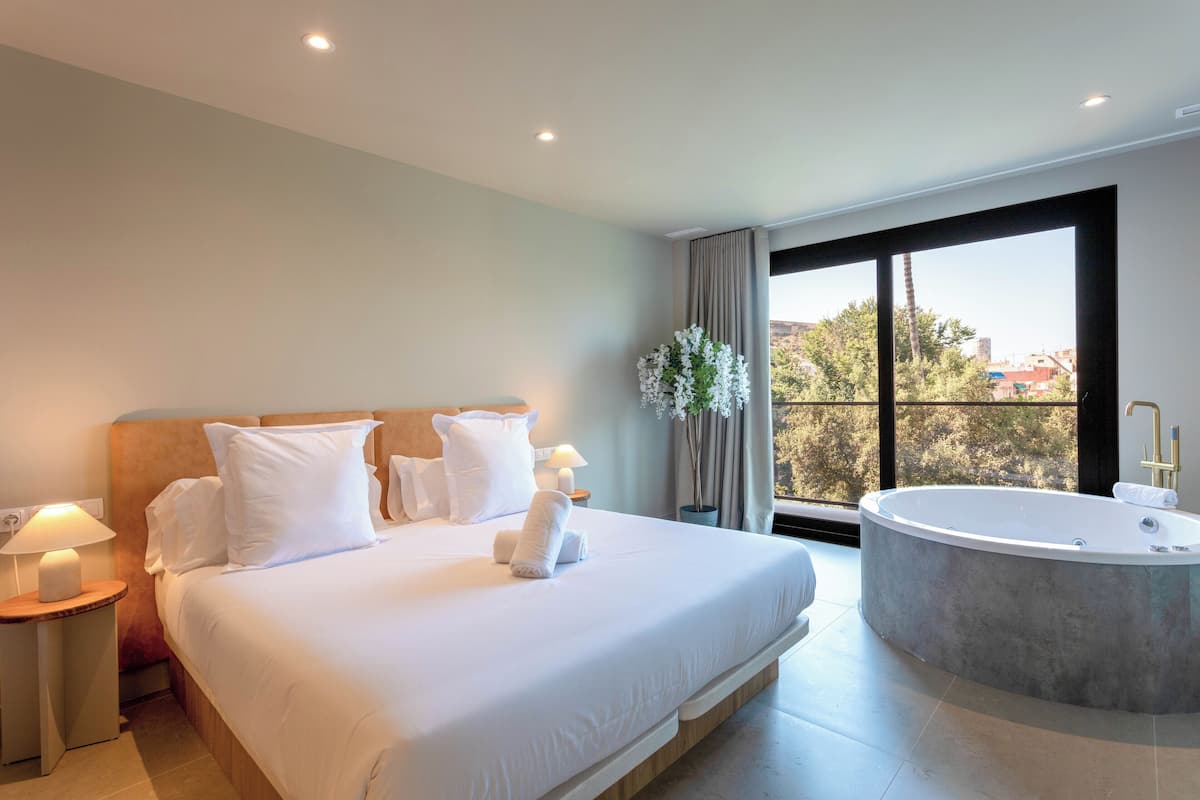 Une chambre d’hôtel moderne dotée d’un grand lit, d’une baignoire et offrant une vue sur la ville grâce à de grandes fenêtres.