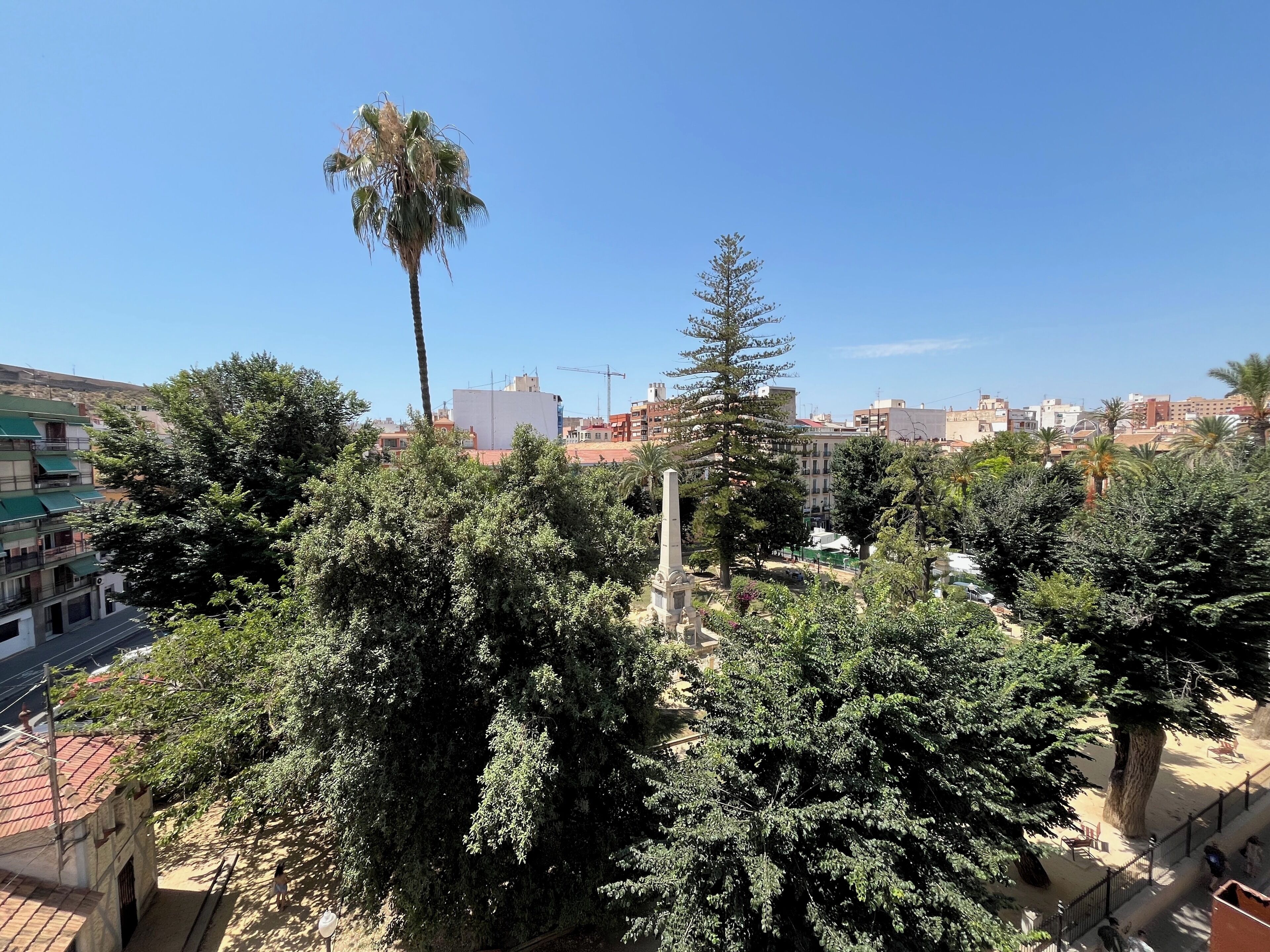 A view of a residential area with trees, a monument, and buildings in the background.