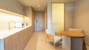 Une cuisine moderne avec un plan de travail blanc, un robinet doré et un four à micro-ondes. On y trouve une chaise en bois et une petite table ronde.