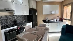 Una cocina moderna con armarios blancos, un refrigerador negro y un comedor con mesa y sillas.