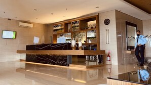 Eine moderne Hotelhalle mit einer Marmor-Rezeption, Holzvertäfelung, einem digitalen Display und einer Wanduhr.