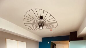 Ein modernes Wohnzimmer mit einem grauen Sofa, einem Holzespeisetisch und gelben Hocker sowie einem Deckenventilator.