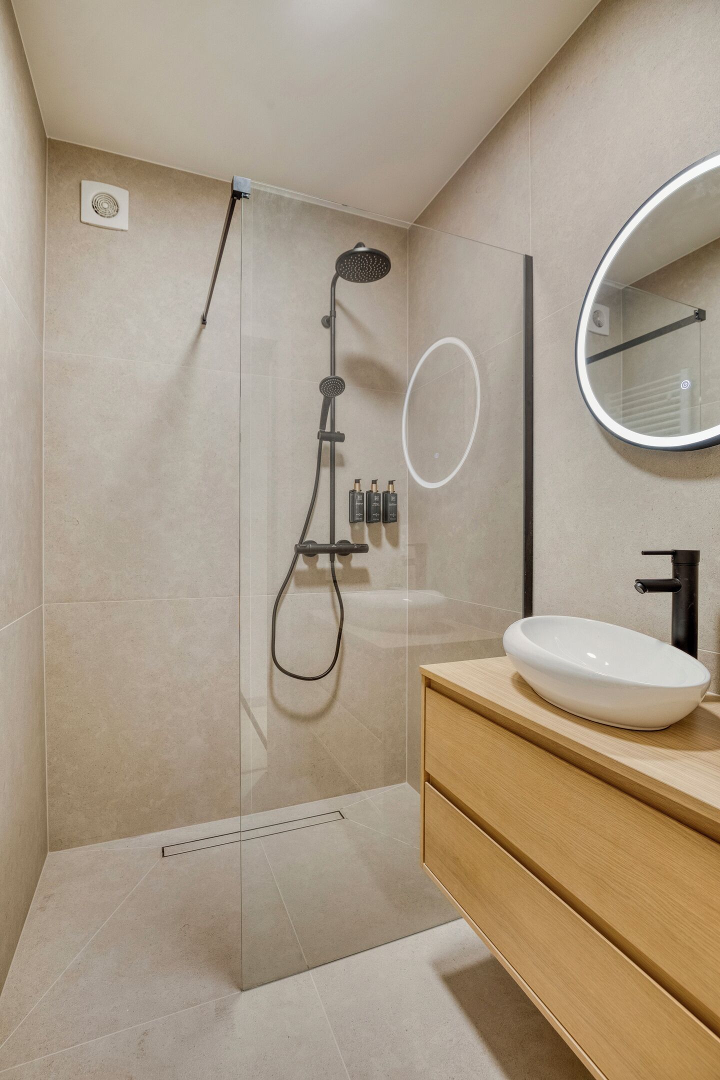 A modern bathroom with a glass-enclosed shower, a wooden vanity with a white sink, and a large mirror.
