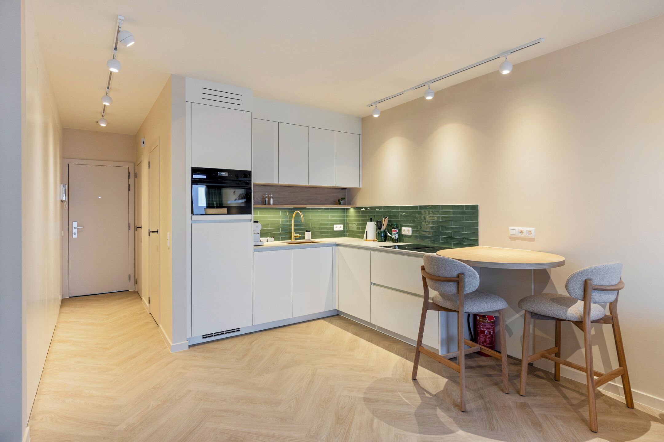 A modern kitchen with white cabinets, a green backsplash, and a round dining table with two chairs.
