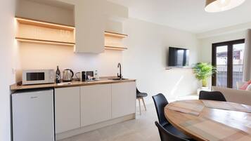 Una cocina moderna equipada con microondas, cafetera y un lavabo. Se observa una mesa de comedor con sillas y un televisor montado en la pared.