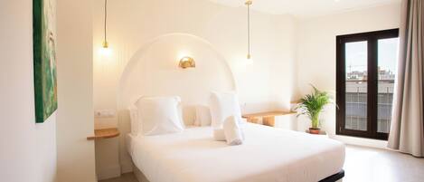 A modern bedroom with a large bed, bedside tables, a potted plant, and a view through a sliding door.