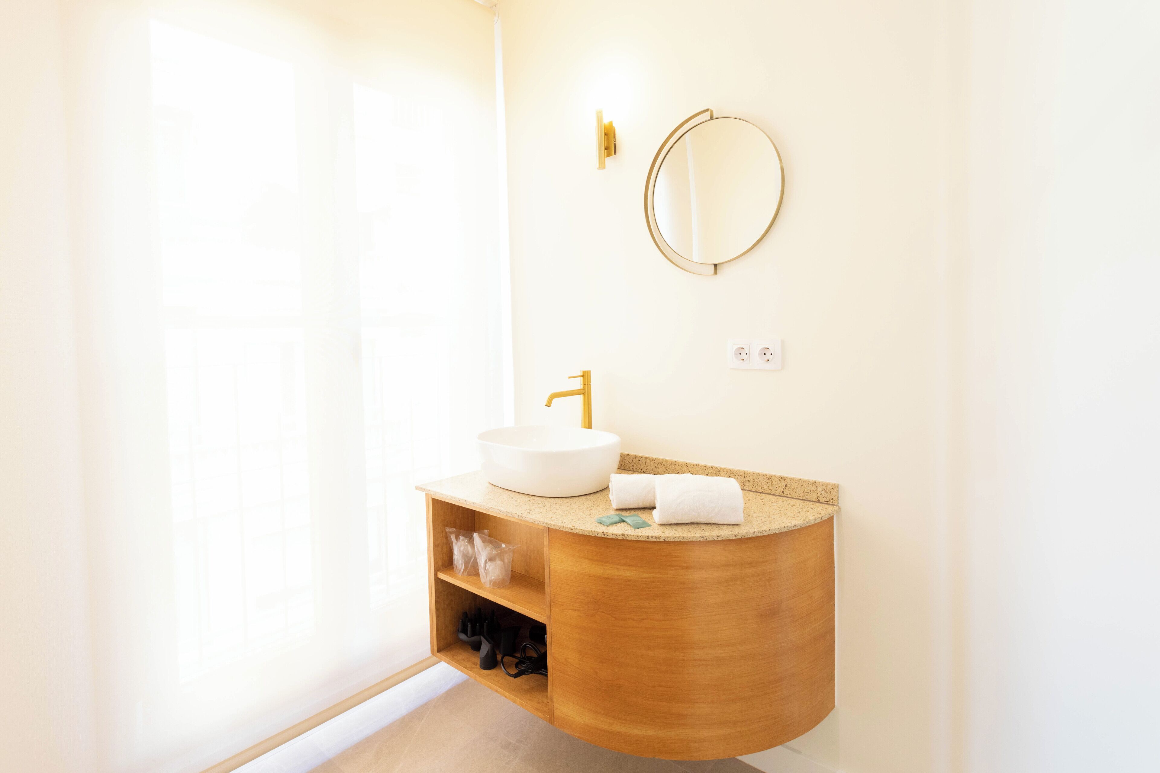 Une salle de bain moderne avec un meuble-lavabo en bois, un miroir rond et un lavabo blanc.