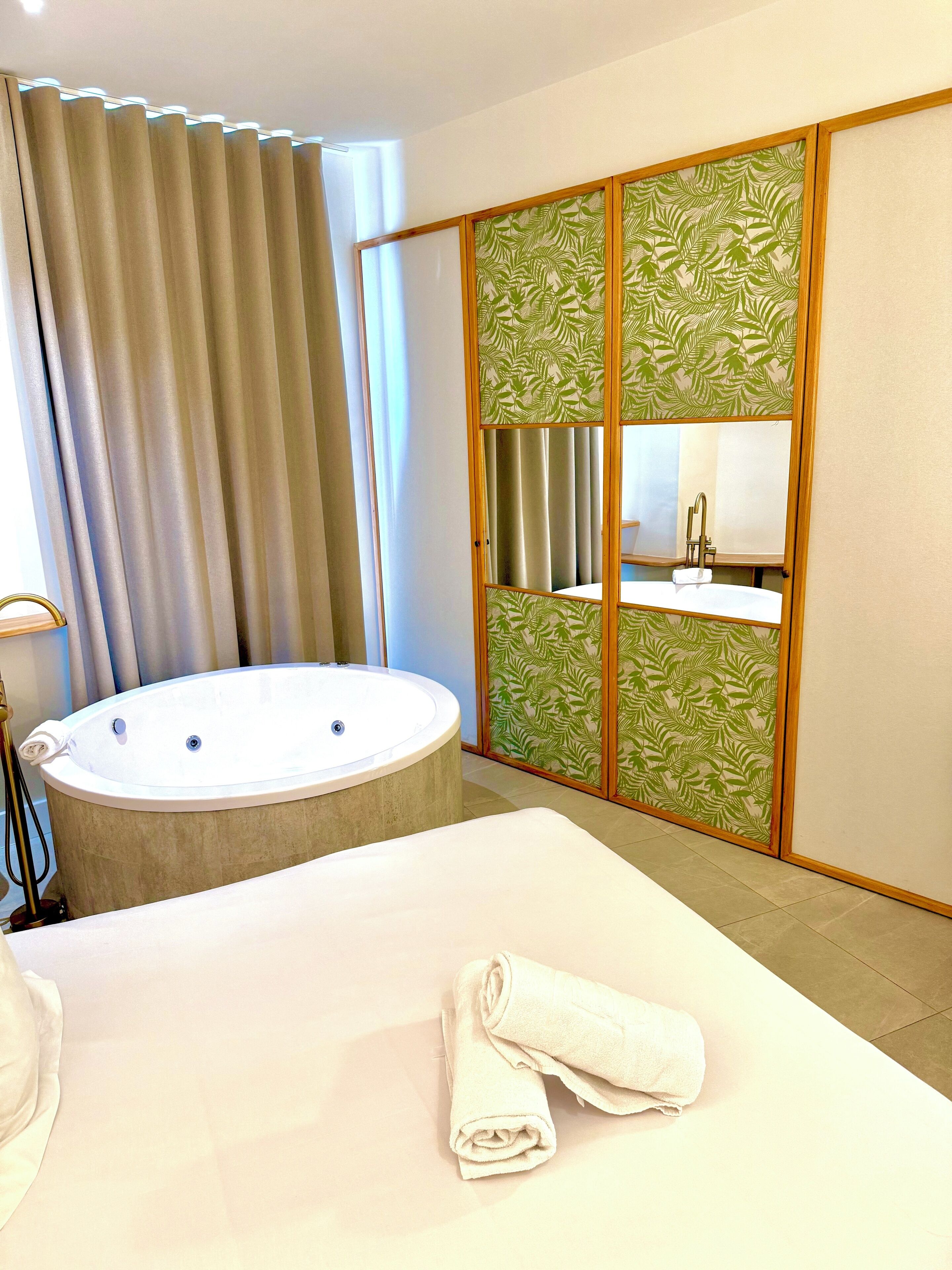 A hotel room with a large bed, a bathtub, and a sliding door with a leaf pattern.