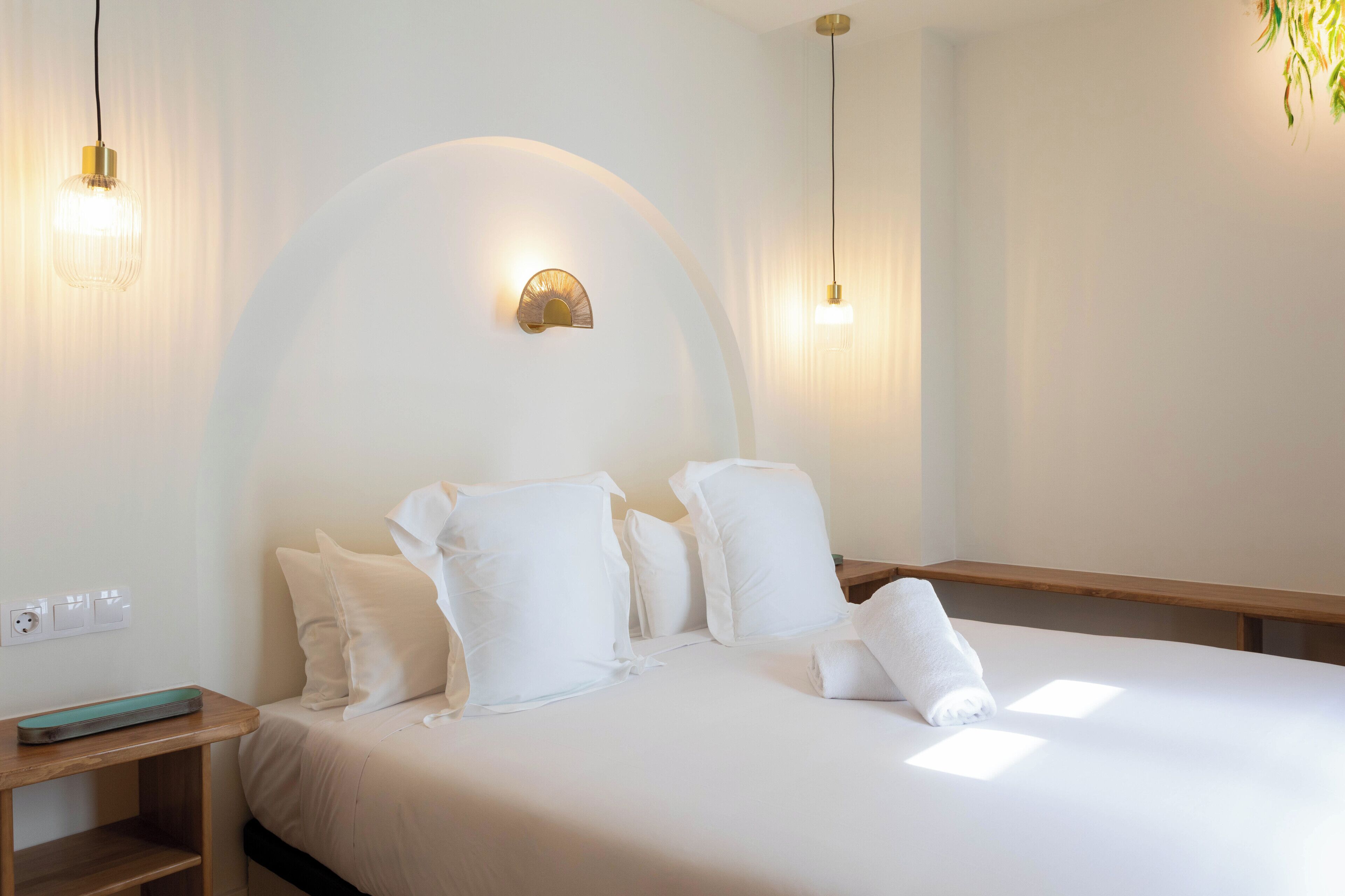 A hotel room with a large bed, white bedding, a wooden nightstand, and a wall-mounted light fixture.