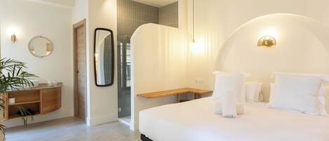 Una habitación de hotel moderna con una cama grande, una mesita de noche, un espejo, un banco de madera y una planta en maceta.