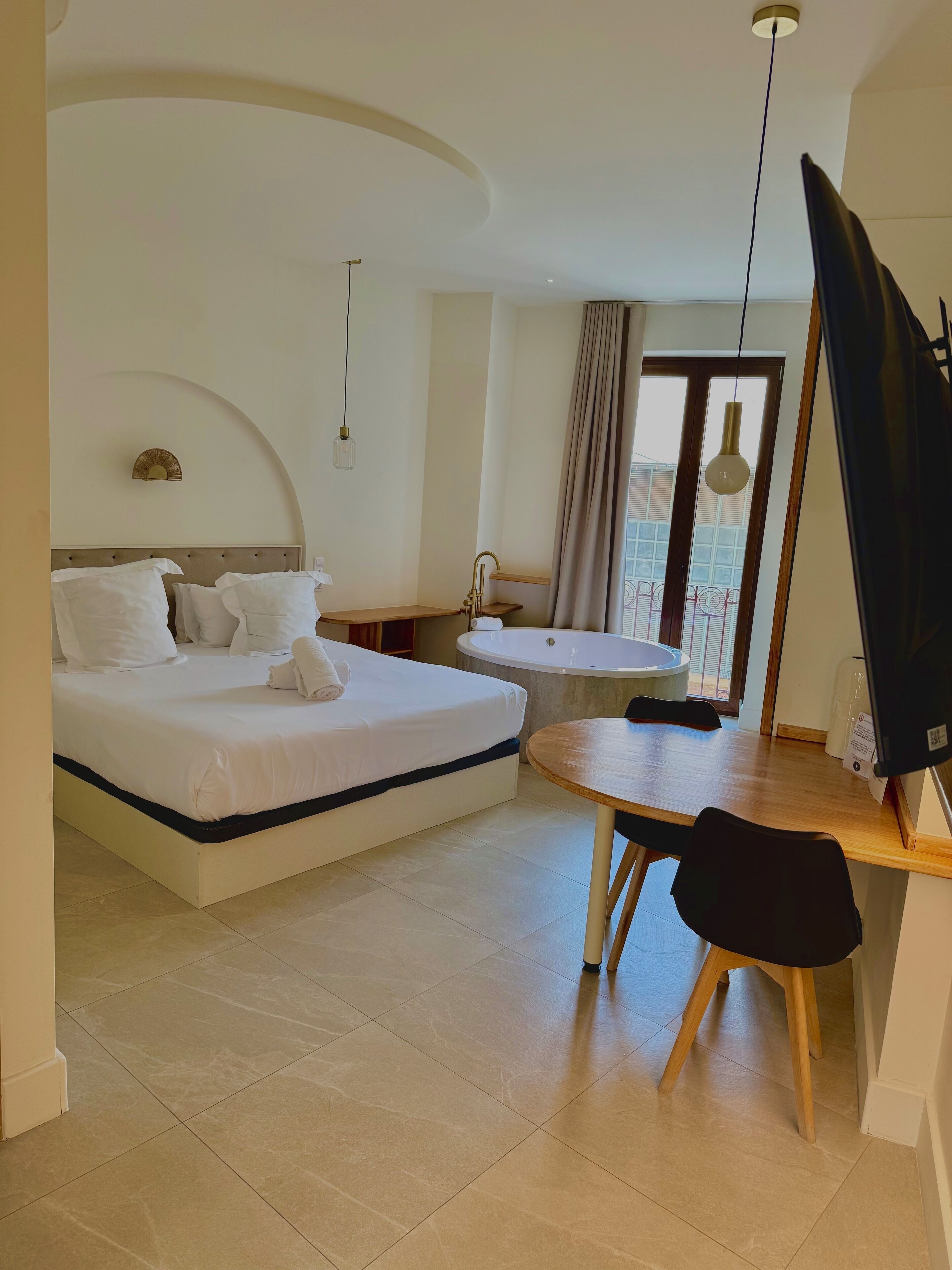 Habitación de hotel con cama, una mesita, televisor y ventana con vistas.