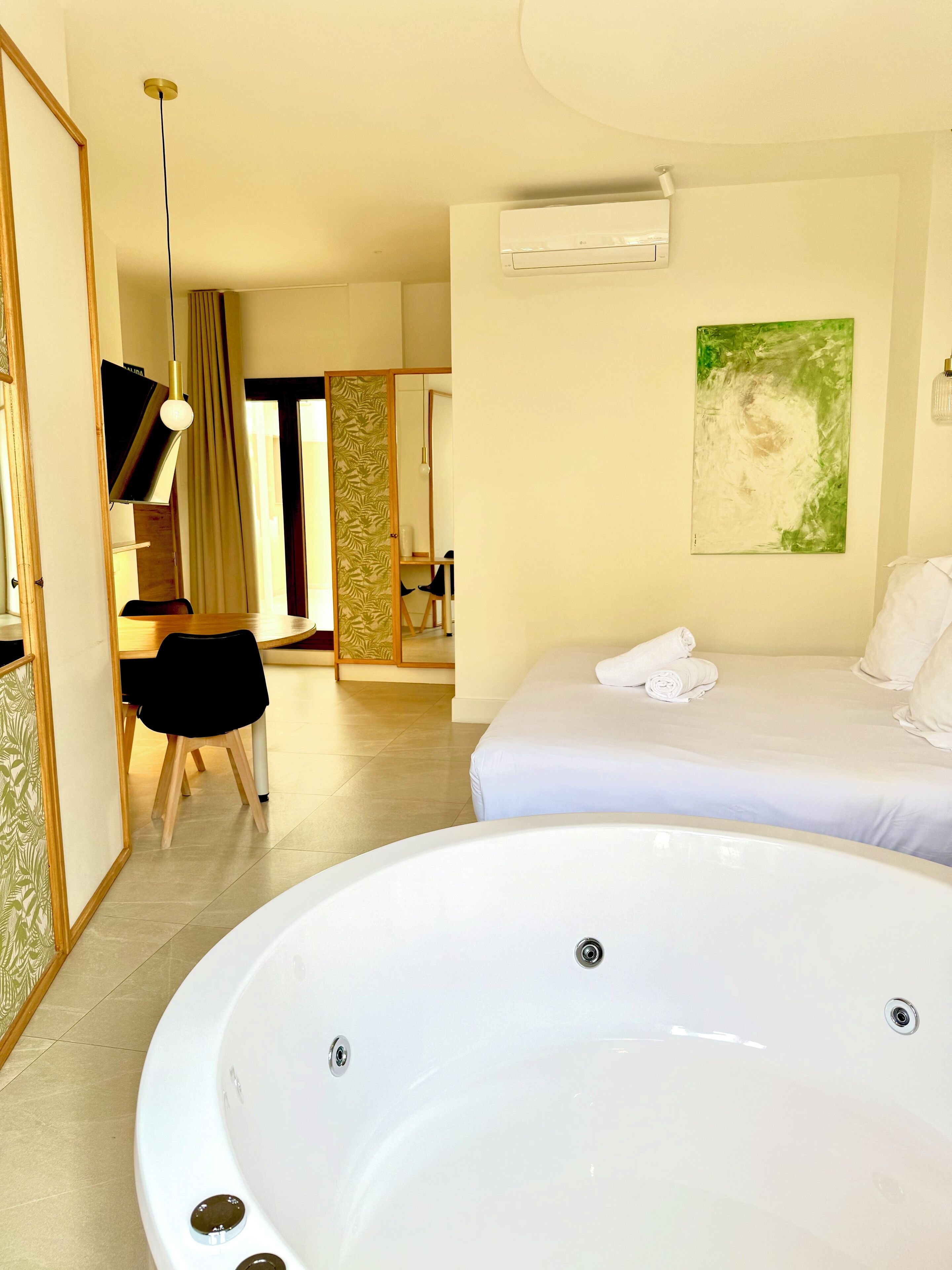 A hotel room with a large bathtub, a bed with white linens, a desk with a chair, and a painting on the wall.