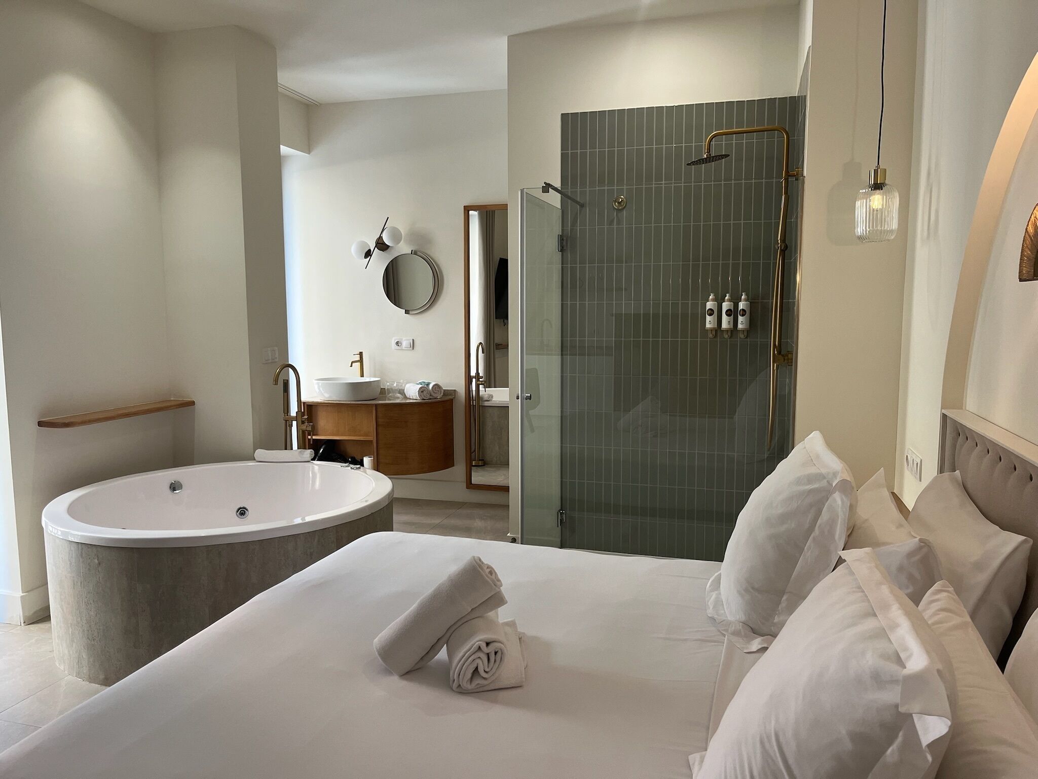 Una habitación de hotel moderna con una cama grande, una bañera, un tocador con espejo y una zona de ducha.