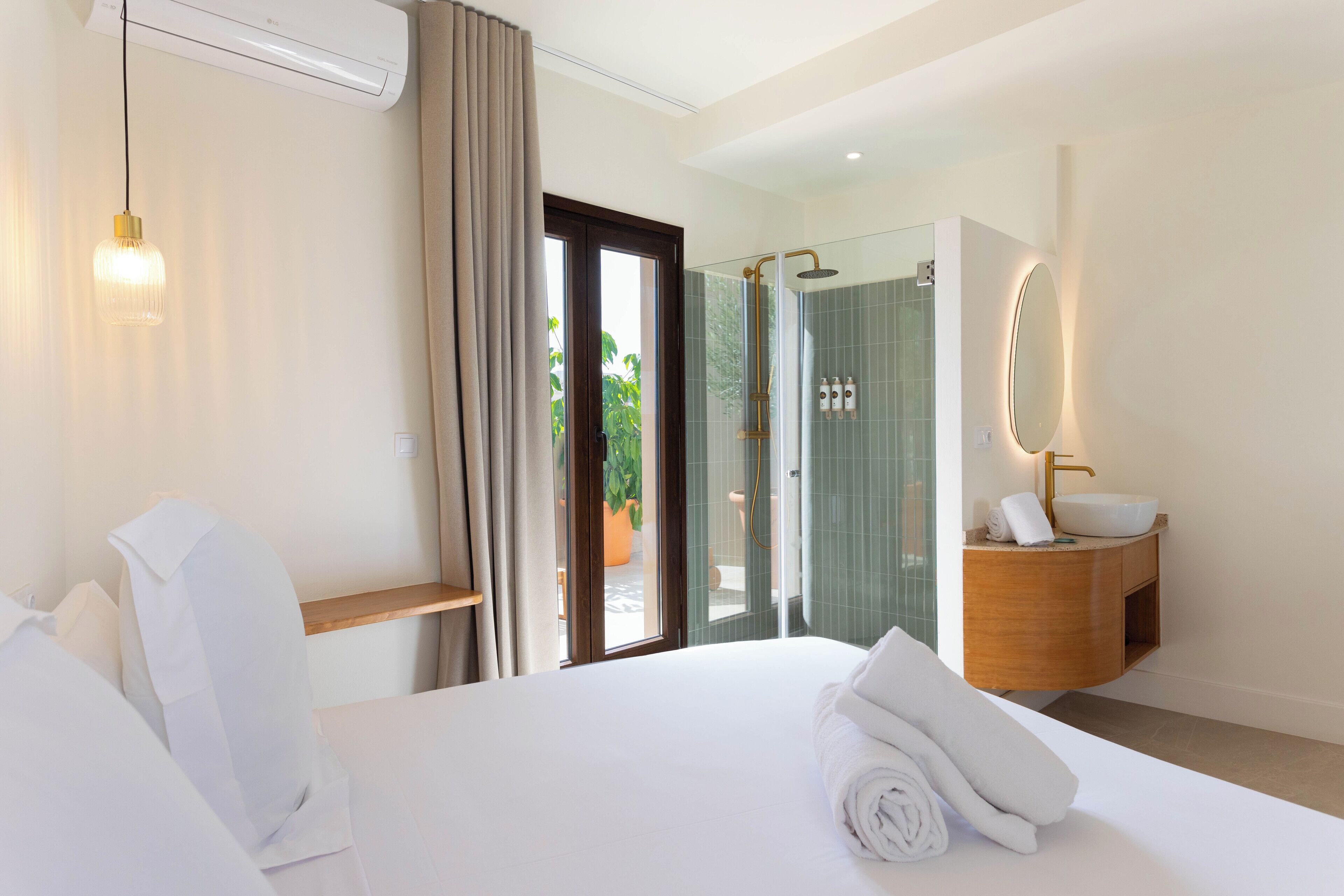 A hotel room with a bed, a bathroom with a sink and mirror, and a sliding glass door to the outside.