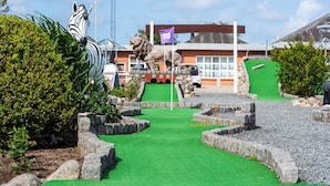A miniature golf course with a zebra statue, a lion statue, and a building in the background. - Rømø familiecamping (Rømø)