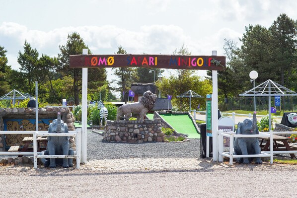 A safari-themed entrance with a lion statue, wooden benches, and a sign reading "ROMO SAFARI MINIGOLF".