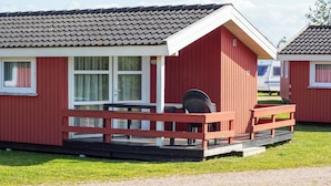 A red building with a white door and windows, a porch with a bench, and a small table. - Rømø familiecamping (Rømø)