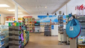 A grocery store with shelves stocked with various products, a checkout area, and a mural of a beach scene on the wall. - Rømø familiecamping (Rømø)
