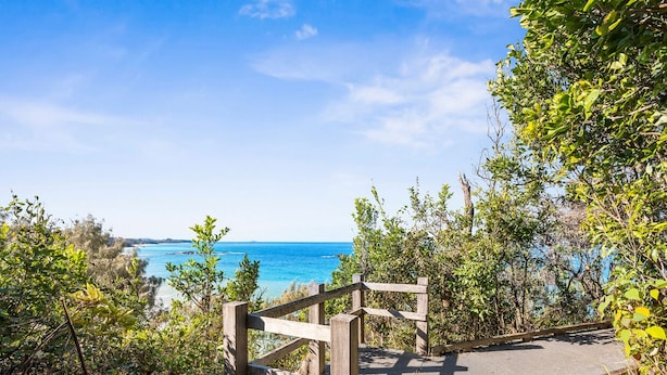 A wooden staircase leading to a beach with clear blue waters and a view of the coastline. - Shell Cove by Charlesworth (Korora)