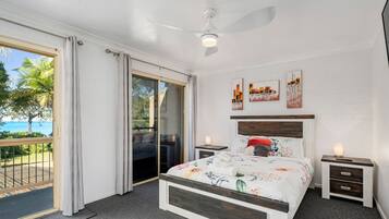 Un dormitorio con una cama, dos mesitas de noche, un ventilador de techo y una obra de arte en la pared.