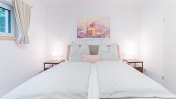 Ein Doppelbett mit gestreifter Bettwäsche, zwei Nachttische mit Lampen, ein Fenster mit Vorhängen und ein Blumenbild an der Wand.