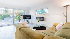 A modern living room with a large TV, a fireplace, and a glass coffee table. - Sund Huus Altefähr - Urlaub im Süden der Insel (Altefähr)
