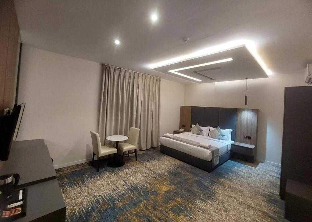 A hotel room with a large bed, a desk, a chair, a small table, and a mirror.