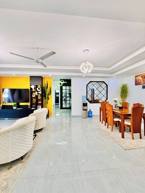 A modern living room with a sofa, dining table, chairs, and a TV. - Modern 3BR Nyali Stay, AC, Kids’ Play Area, Pool, Gym & 3 Min to Beach (Mombasa)