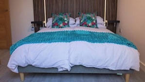Una cama con colcha verde aguamarina y blanca, dos almohadas florales y un cabecero de listones de madera.