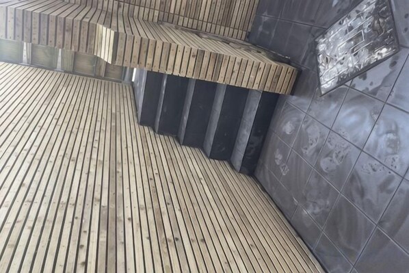 A wooden slatted floor leading to a dark tiled wall with a metallic plaque. - Sunbeam House Apartment 1 (Heysham)