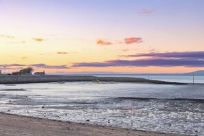 A coastal landscape with a sunset, a body of water, and a distant shoreline. - Sunbeam House Apartment 1 (Heysham)