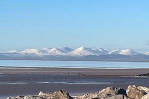 Une plage avec un rivage rocheux et, au loin, des montagnes enneigées.