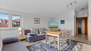 Una sala de estar moderna con un sofá, un televisor, una mesa de comedor con sillas y vistas al exterior.