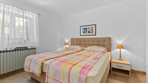 Ein Schlafzimmer mit einem Bett, zwei Nachttischlampen, einer Heizung und einem Fenster mit durchsichtigen Vorhängen.