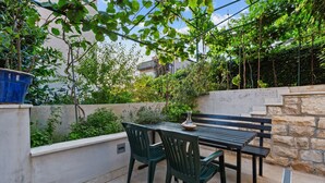 Eine Terrassengrundstück mit Tisch und Stühlen, umgeben von viel Grün und einer Steinmauer.