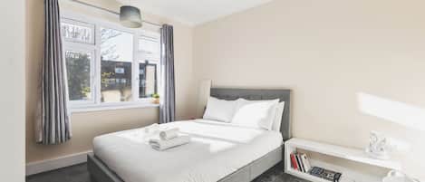 A hotel room with a bed, bedside table, and a window with curtains.