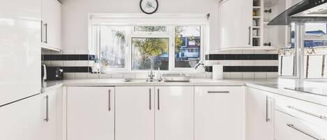 A modern kitchen with white cabinetry, a large window, and a visible clock.