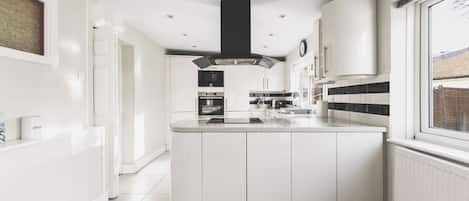 A modern kitchen with white cabinetry, a central island, and a black range hood.