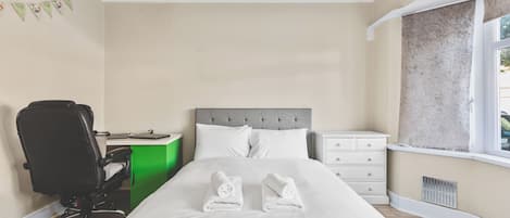 A bedroom with a bed, a desk, a chair, and a window.