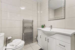 Een moderne badkamer met toilet, een handdoekhouder, een wastafel met spiegel erboven en een douchehoek.