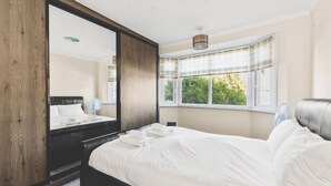 Una camera da letto con un grande specchio, un letto con lenzuola bianche, un comodino e una finestra con tende.