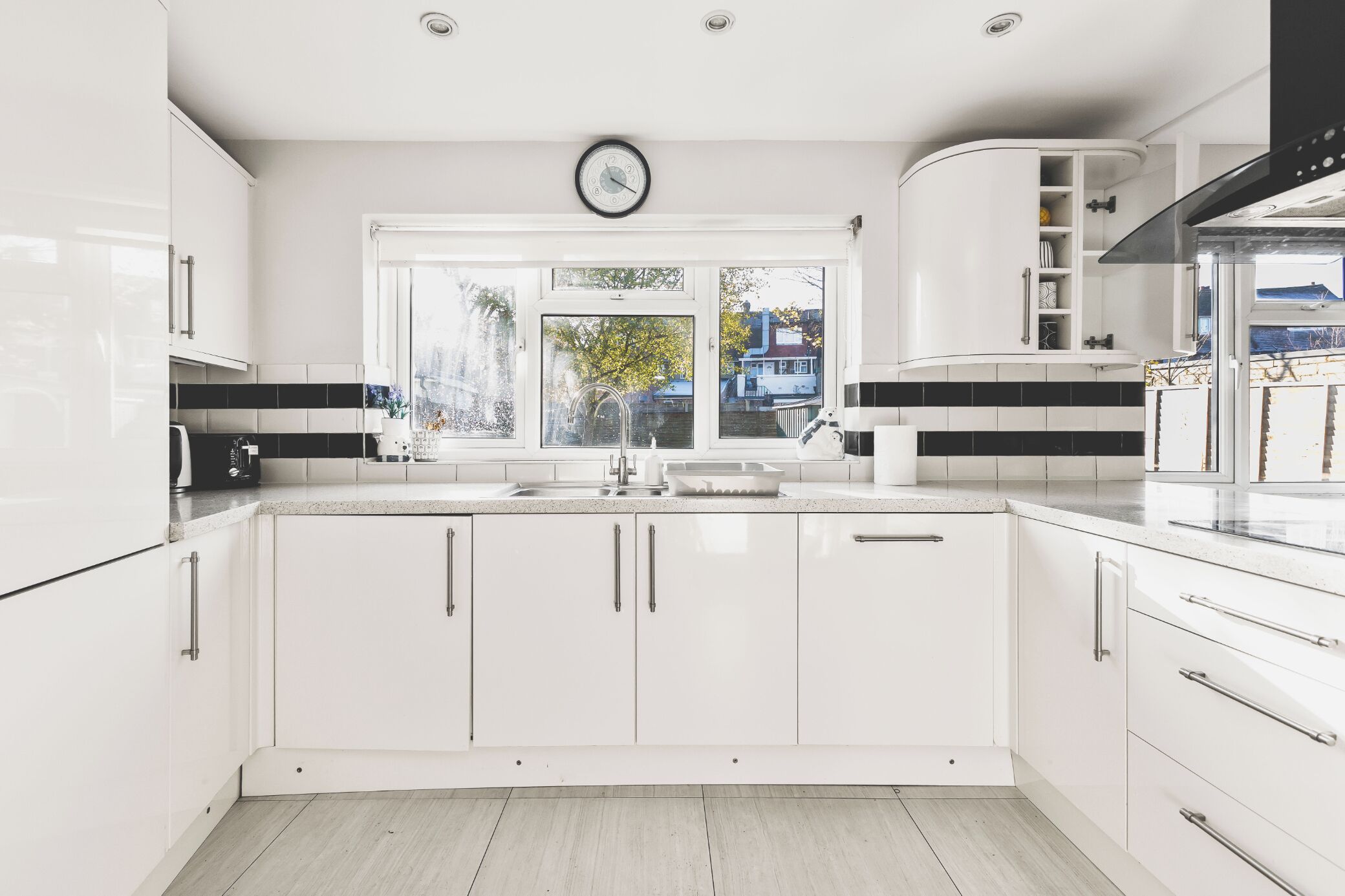 A modern kitchen with white cabinetry, a large window, and a visible clock.