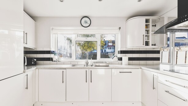 Una cocina moderna con armarios blancos, un ventanal grande y un reloj a la vista.