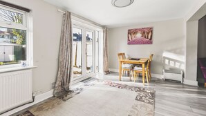 Una habitación con una mesa de comedor, sillas, un radiador, una ventana con cortinas y una lámpara en el techo.