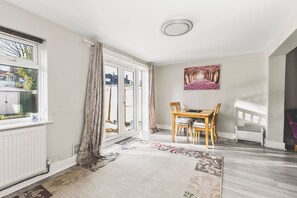 A room with a dining table, chairs, a radiator, a window with curtains, and a ceiling light. - Spacious 4BDR House with Parking by Heathrow (Greater London)