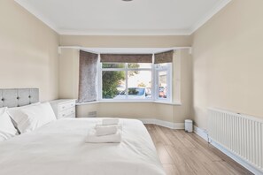 Un dormitorio con una cama grande, una ventana con cortinas, un radiador y vistas al exterior.