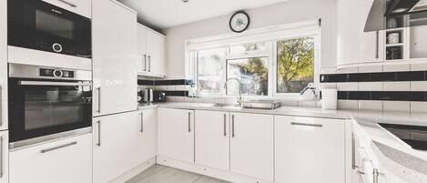 A modern kitchen with white cabinetry, a Bosch oven, a sink, and a window with a view of trees.