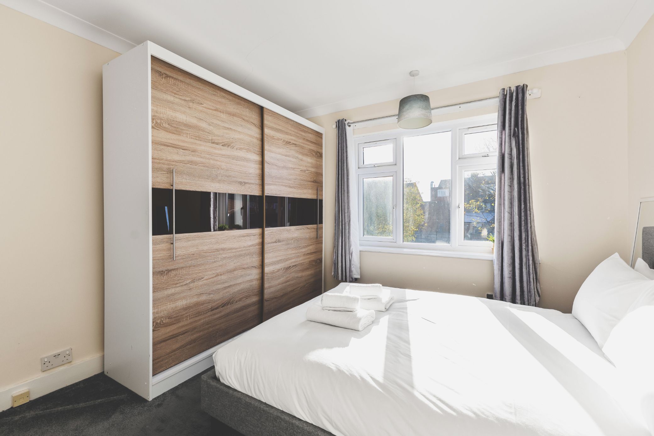 A bedroom with a bed, a wardrobe, a window with curtains, and a pendant light.