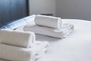 Een net opgemaakt bed met opgerolde witte handdoeken.